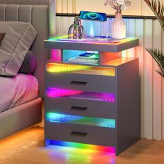 a night stand with multicolored drawers and lights on the bottom shelf next to a bed