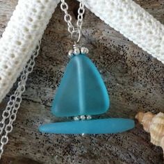 a necklace with a blue glass triangle on it and a seashell in the background