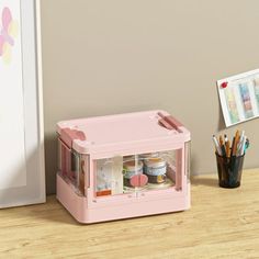 a small pink toy refrigerator sitting on top of a wooden table next to a cup