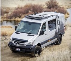 a white van driving down a dirt road next to a body of water and dry grass