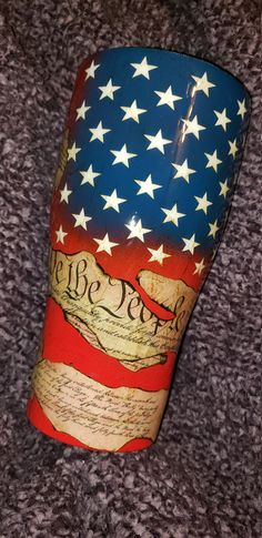 an american flag cup with the words we the people written on it, sitting on a carpet