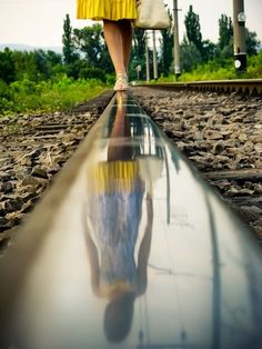 a person standing on train tracks with their reflection in the water