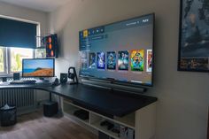 a computer desk with two monitors and a keyboard in front of a large screen monitor