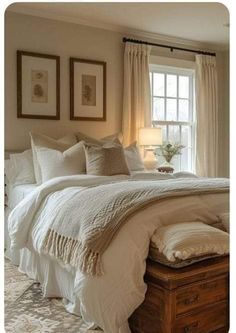 a white bed sitting under a window next to a wooden trunk with pillows on it