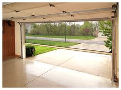 an open garage door in front of a driveway with grass and trees on the other side