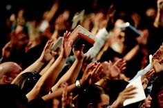 a group of people with their hands up in the air and one person holding a book