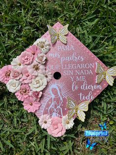 a pink graduation cap with flowers and butterflies on the top is laying in the grass