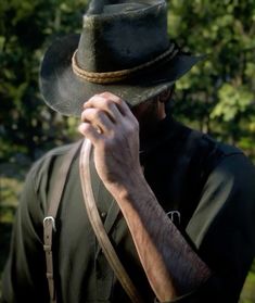 a man wearing a hat and holding his hand up to his face with trees in the background