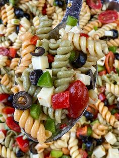 a spoon full of pasta salad with olives, tomatoes, and other toppings