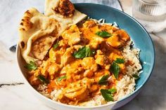 a bowl filled with rice and chicken curry next to pita bread on a table