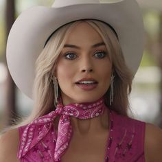 a woman with blonde hair wearing a pink shirt and cowboy hat, looking at the camera