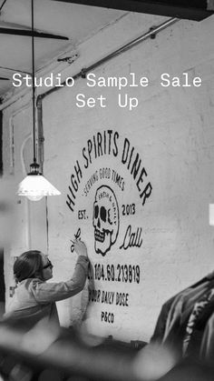 a man is painting the side of a wall with a skull on it and other people are sitting in chairs