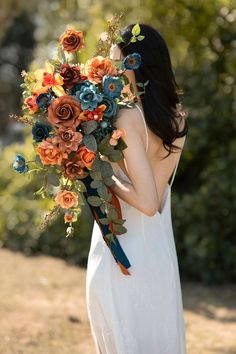 a woman in a white dress holding a bouquet of orange, blue and red flowers