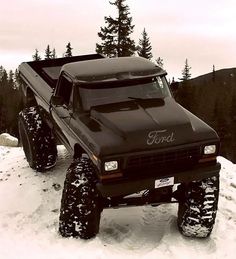 a black truck with large tires on top of snow covered ground