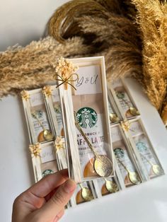 a person holding a starbucks cup and spoon in front of some fake gold leaf decorations