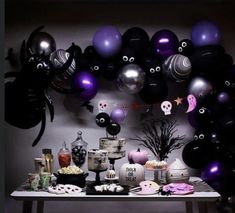 a table topped with lots of black and purple balloons next to a wall covered in halloween decorations