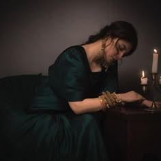 a woman in a green dress sitting next to a candle