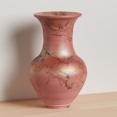 a pink vase sitting on top of a wooden table next to a white wall in the background