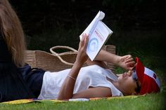 a woman laying on the grass reading a book with her legs up in the air