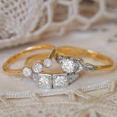 two gold and white diamond rings sitting on top of a lace covered table cloth next to each other