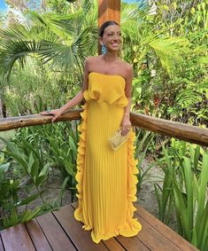 a woman wearing a yellow dress standing on a wooden deck with palm trees in the background