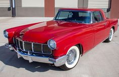 an old red car parked in front of a building