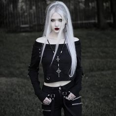 a woman with white hair and makeup wearing black clothing in front of a grassy area