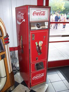 an old coca - cola machine sitting in front of a window