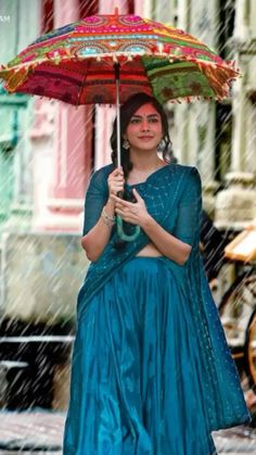 a woman is walking in the rain holding an umbrella and wearing a blue sari