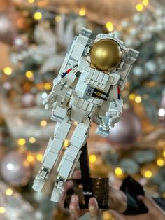 a person holding up a lego space suit in front of a christmas tree with lights