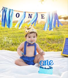 a baby wearing a birthday hat sitting in front of a blue cake with the number one on it