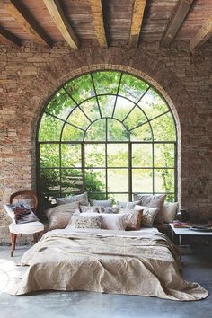 a bedroom with an arched window and stone walls, along with pillows on the bed