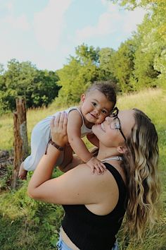 a woman holding a baby in her arms while standing next to a fence and trees