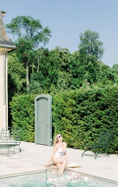 a woman sitting on the edge of a swimming pool in front of a green building