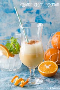 an orange drink in a glass next to sliced oranges on a blue tablecloth