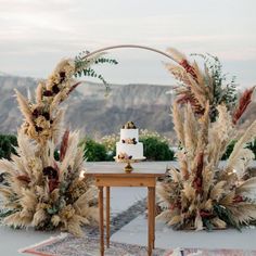 a table with a cake sitting on top of it next to some flowers and plants