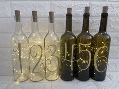 three wine bottles with the number twenty six on them are decorated with string lights and sit in front of a white brick wall