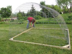 a man bending over in the middle of a garden with a large metal structure behind him