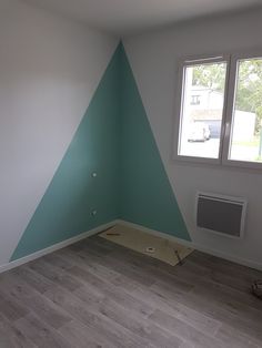 an empty room with blue and white paint on the walls, wood flooring in front of a window