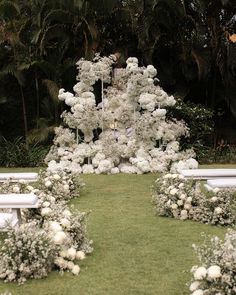 an arrangement of white flowers and benches in the middle of a grassy area with palm trees