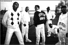 black and white photograph of four men in baseball uniforms, one wearing a jacket with argyle print on it