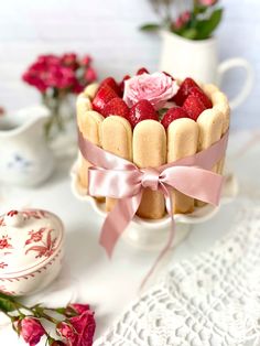 a cake with strawberries on top and pink ribbon tied around the edges sitting on a table