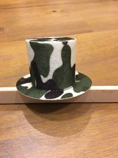 a green and white camo hat sitting on top of a wooden table next to a piece of wood