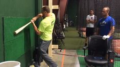 a man holding a baseball bat while standing next to a green wall in a batting cage