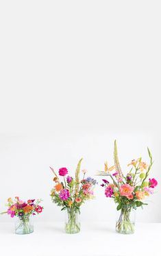 three vases filled with colorful flowers on top of a white countertop next to each other