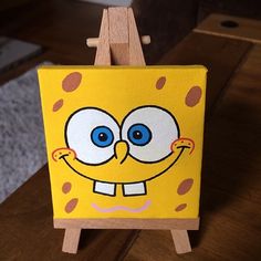 a yellow cartoon character painted on an easel with blue eyes and brown polka dots