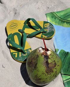 a green coconut sitting on top of a beach next to a pair of flip flops