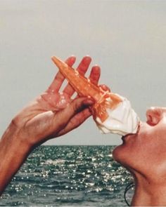 a person is eating something out of their hand near the ocean water with his mouth open