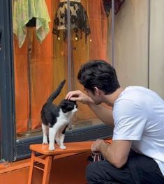 a man petting a black and white cat in front of a store window