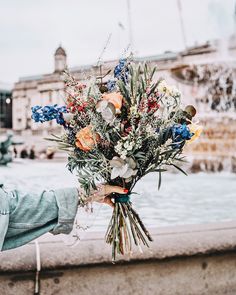 a person holding a bouquet of flowers in front of a fountain